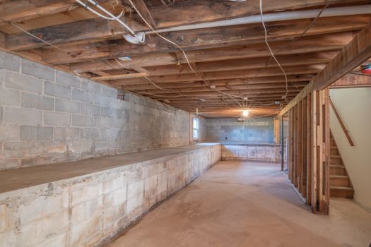 Empty basement with exposed wooden beams, concrete walls and stairs.